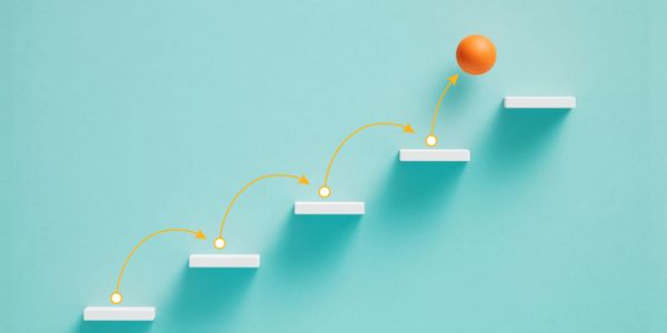 Orange ball hopping up white steps symbolizing progress.