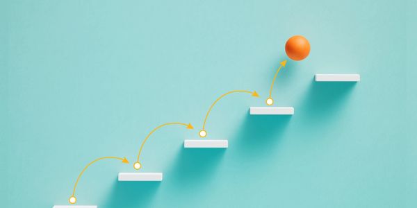 Orange ball hopping up white steps symbolizing progress.