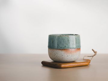 A ceramic cup with green and speckled design on a wooden coaster.