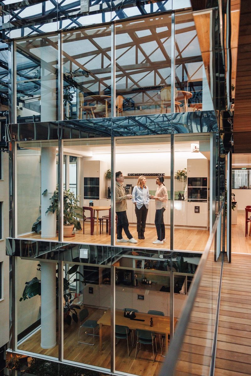 A group of confident male and female business professionals of diverse ethnicities engage in discussion in a chic office cafe space, reflecting contemporary corporate collaboration.