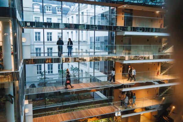 People walking inside a modern multi-level building with glass railings.