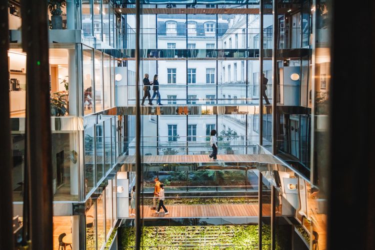 People walking on glass corridors inside a modern office building with greenery below.