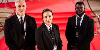Três seguranças em traje formal em um tapete vermelho.