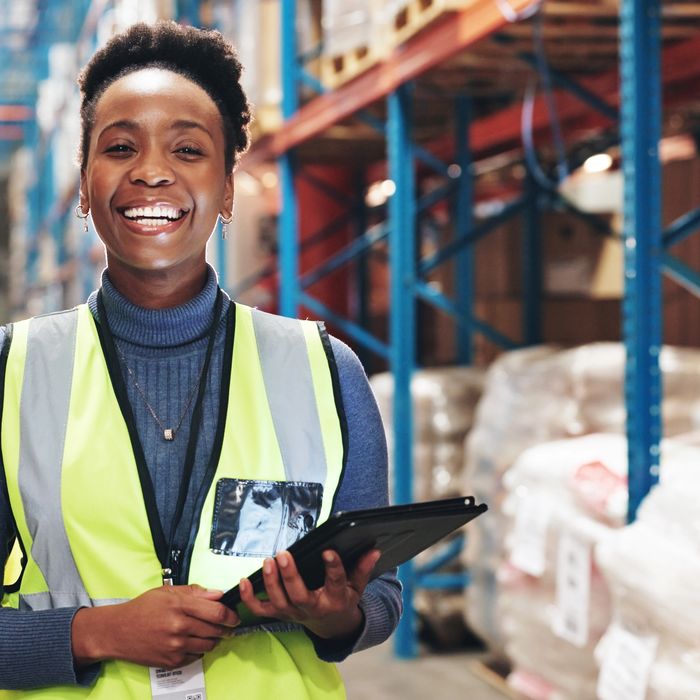 Smiling warehouse worker wearing a safety vest and holding a tablet.