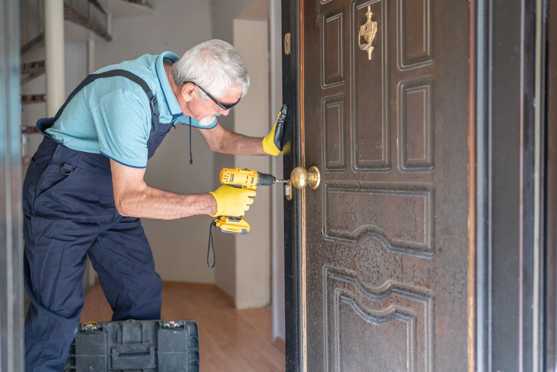 An elderly man installing a door lock with a power drill.