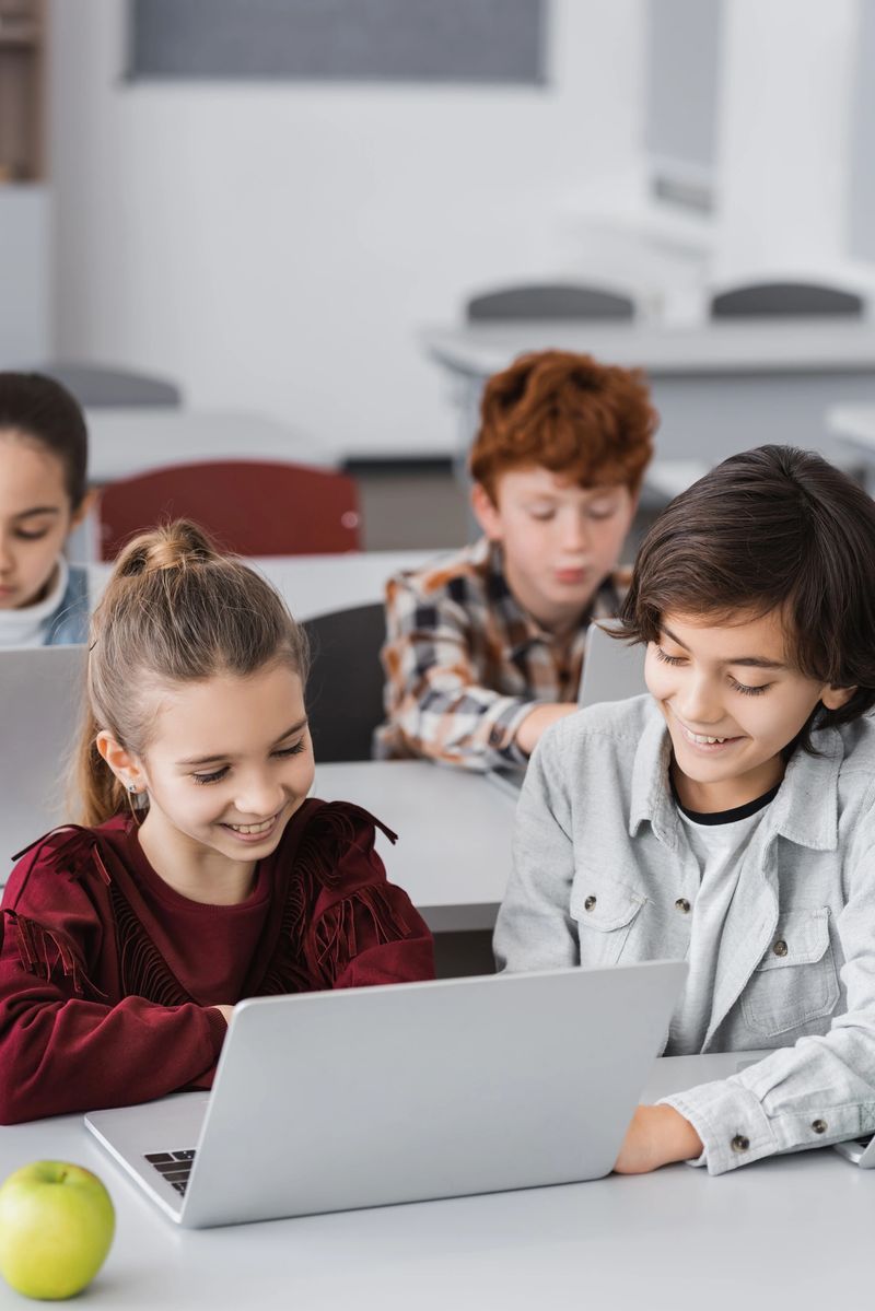 A group of enthusiastic schoolchildren work together on a laptop, sharing ideas and knowledge in class.