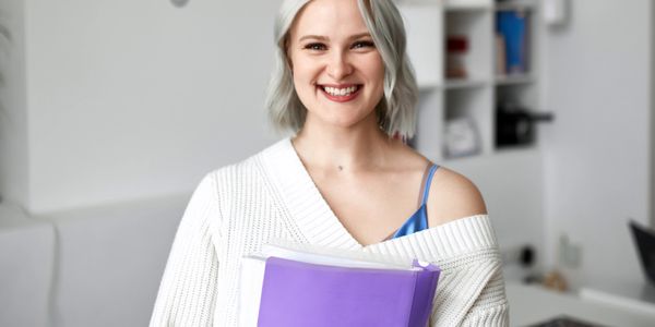 Smiling woman holding purple folder in a cozy white sweater.
