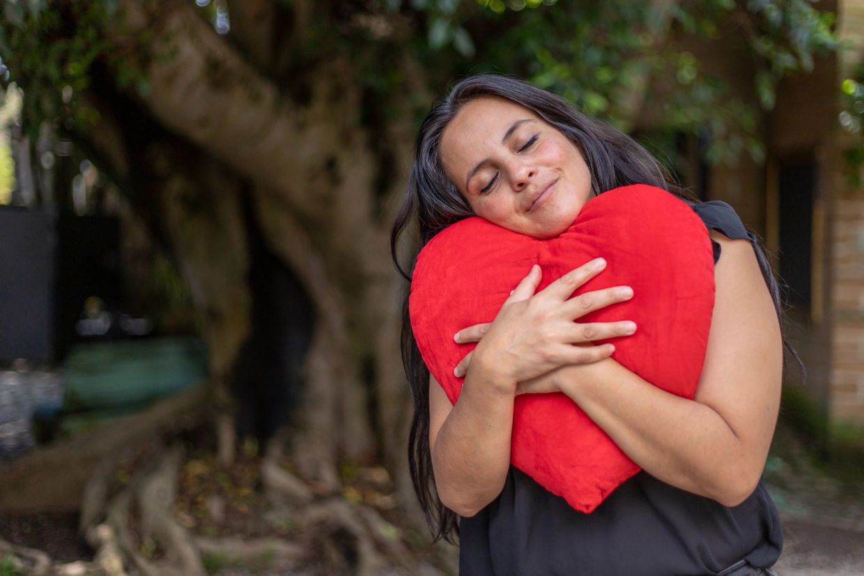 Woman hugging a red heart-shaped pillow with eyes closed.