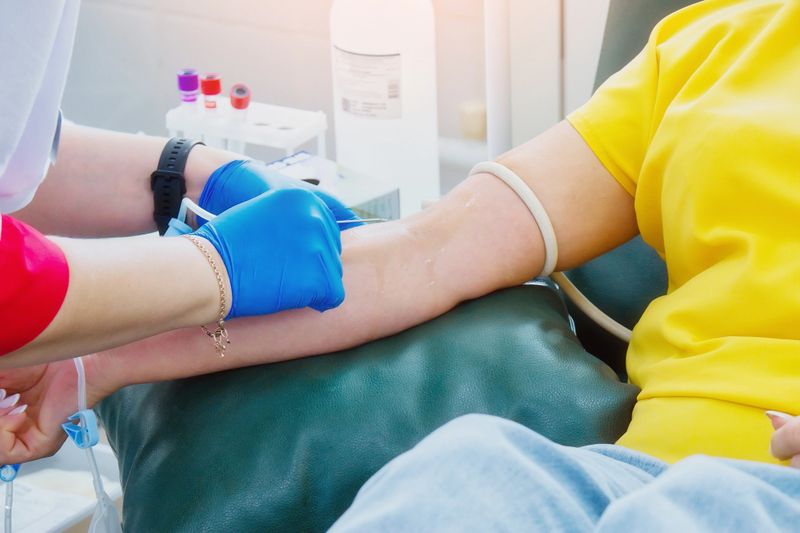 A healthcare professional wearing gloves is seen inserting a needle into a person's arm to collect blood, showcasing a medical procedure in a clinical setting with a focus on patient care.