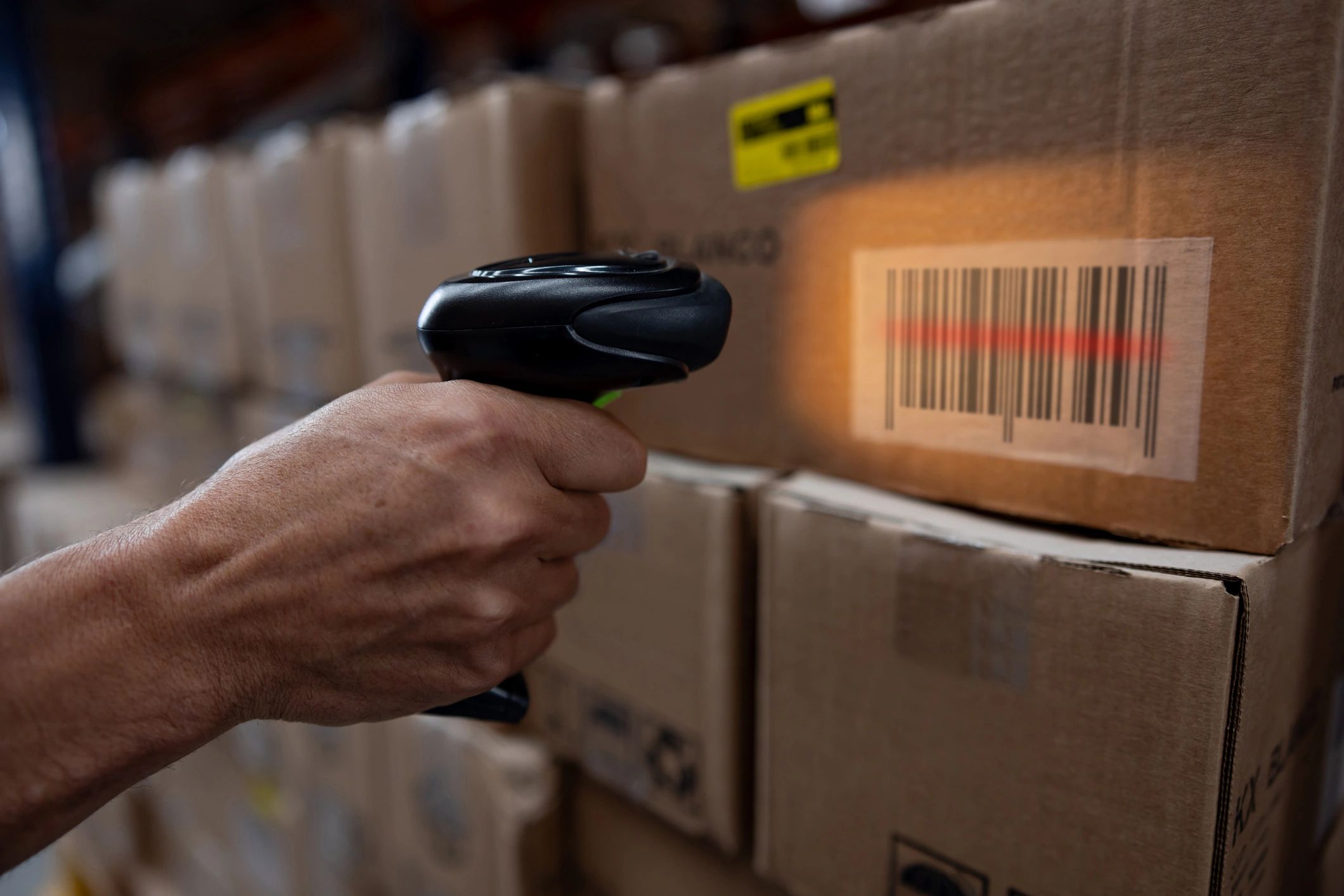 Hand scanning barcode on cardboard box in warehouse.