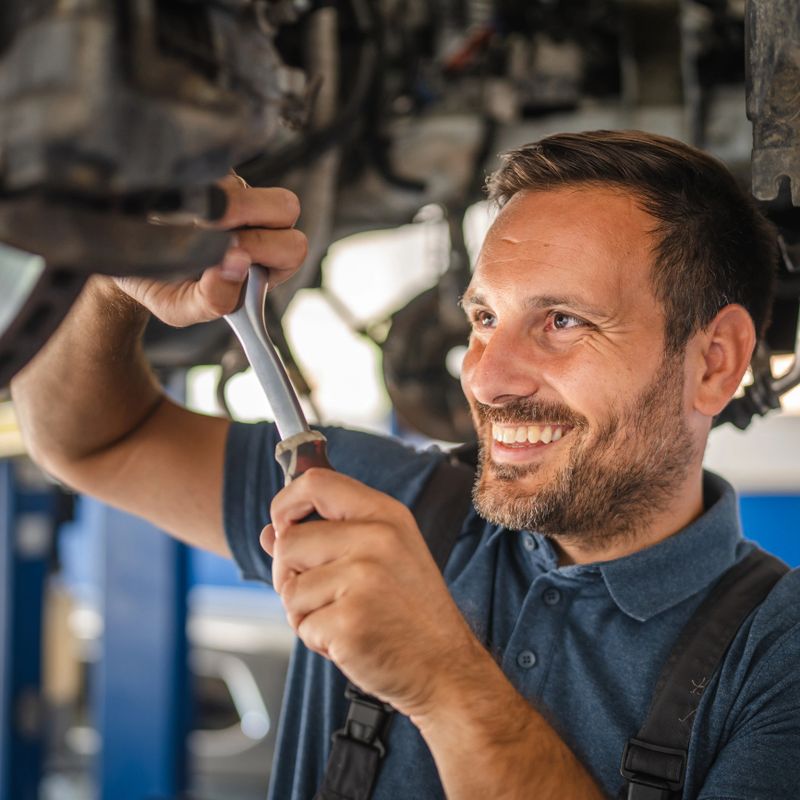 Car mechanic fix the undercarriage of a vehicle, indicating the practical work involved in automotive repair and maintenance for optimal performance