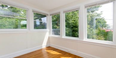 Empty corner room with large windows and wooden floor.