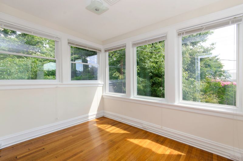 A bright sunroom with large windows and a wooden floor allows natural light to flood the space, offering a cozy spot to enjoy the outdoors from within.