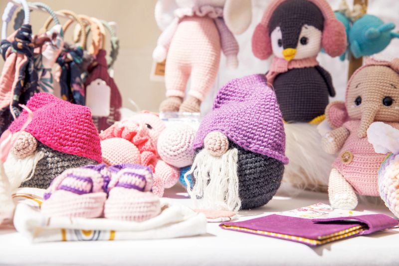 Colorful handmade crocheted toys, gnomes, animals, displayed at a craft fair, bright colors, detailed, focus on craftsmanship, playful environment, handmade crafts concept