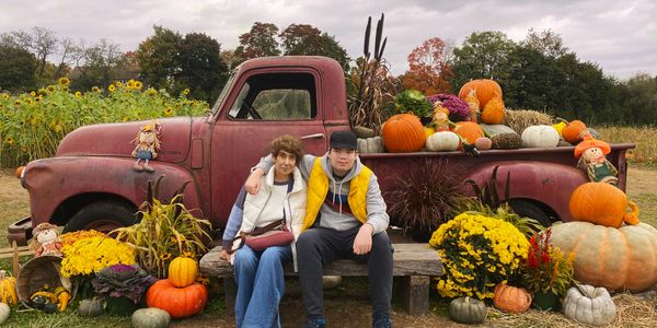 Two people sitting on a bench in front of a vintage truck decorated with pumpkins and autumn flowers.