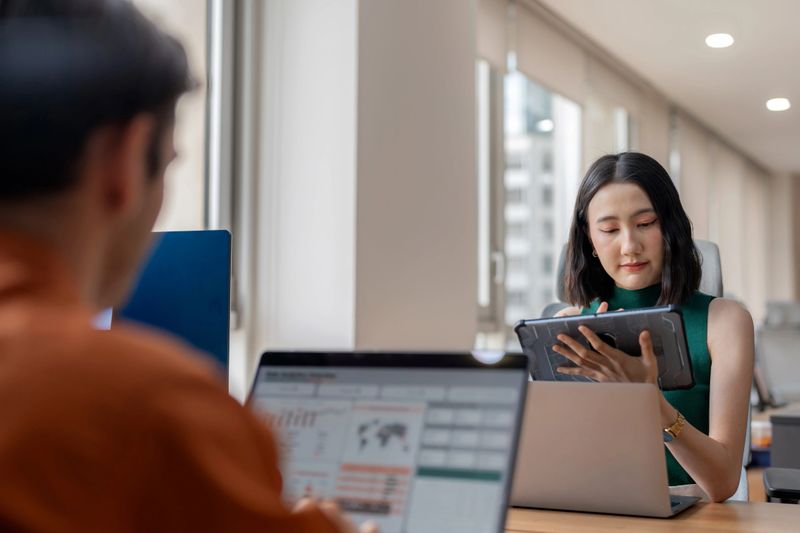 A diverse business team utilizes data analytics to predict market trends during a strategy meeting in a modern office. Team members collaborate, using laptops and digital displays to analyze key factors influencing business success. Business processes, leadership, and innovative problem-solving.