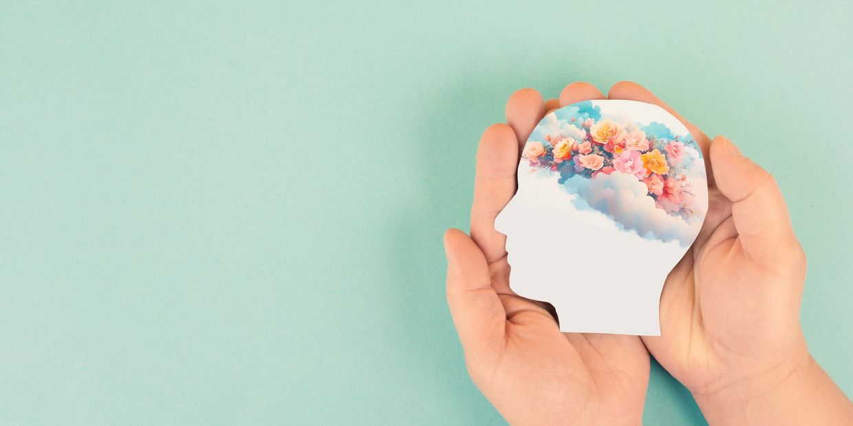 Hands holding a cutout of a head filled with colorful flowers and clouds.
