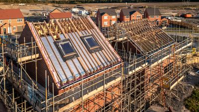 Two houses under construction with visible wooden roof framing and scaffolding.
