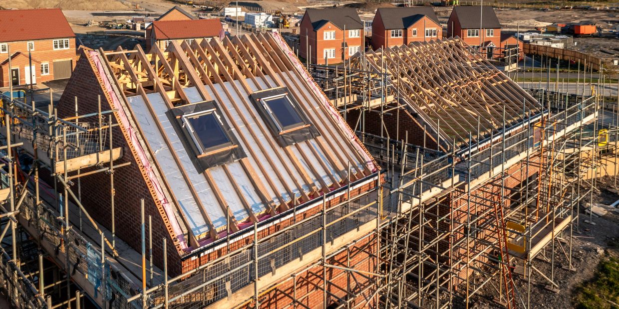 Two houses under construction with wooden roof frames and scaffolding.