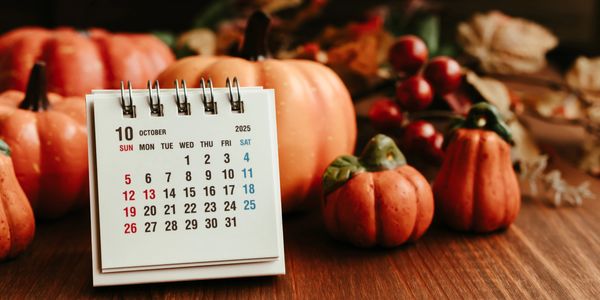 October 2025 calendar with decorative pumpkins on wooden table.