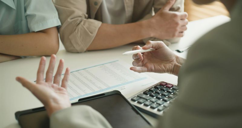 Business meeting with clients reviewing financial documents and strategies. Hands gesturing emphasize communication and collaboration. Calculator and documents on the table indicate focus on finance.