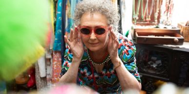 Elderly woman wearing red sunglasses and colorful outfit.