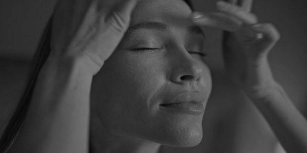 Close-up of a woman with closed eyes, touching her face gently.