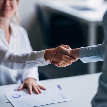 Two professionals shaking hands over a desk with documents.