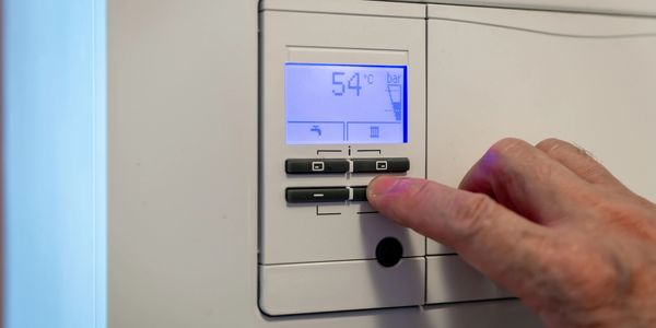 Hand adjusting temperature on a digital thermostat showing 54°C.