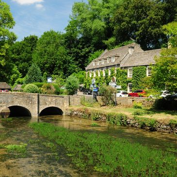 Stone bridge over a clear river with a house and trees.