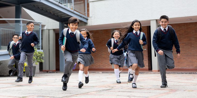 Group of schoolchildren running happily outside their school building.
