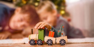 Children play with a wooden toy train near a Christmas tree.