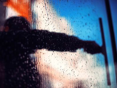 Window cleaner using squeegee on wet glass with sky reflection – professional window cleaning