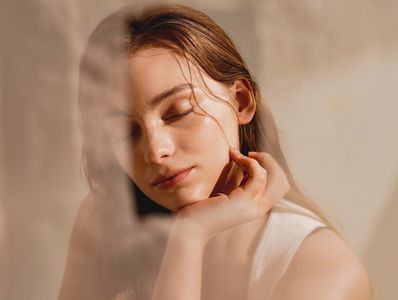 A serene woman with closed eyes and a gentle touch on her face.