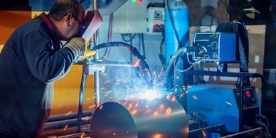 A man welding a large metal cylinder in a workshop.