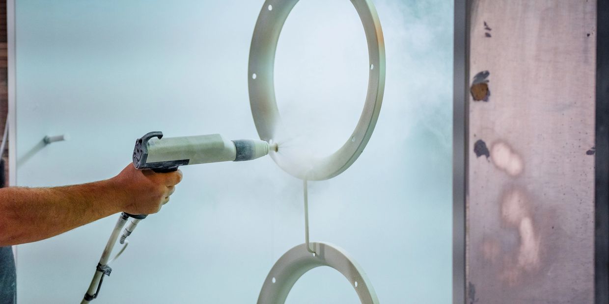 A hand spray-painting circular metal parts in a workshop.