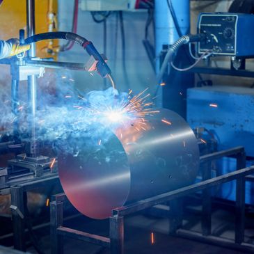 Robotic arm welding a metal cylinder in an industrial setting.