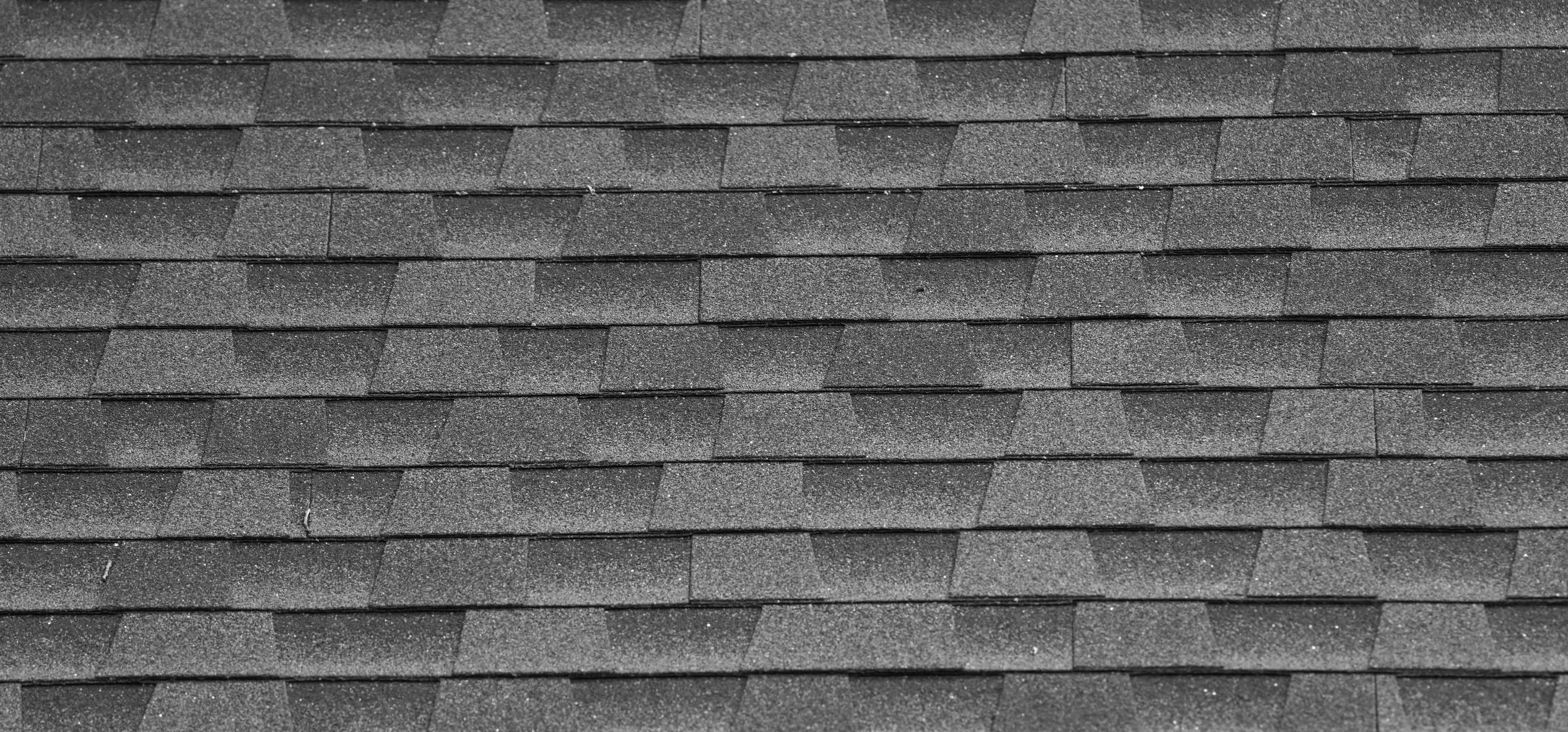Close-up of dark gray asphalt roof shingles arranged uniformly.