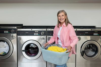 Smiling woman carrying a laundry basket in a laundromat.