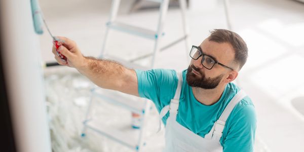 Man in glasses painting a wall with a roller brush indoors.
