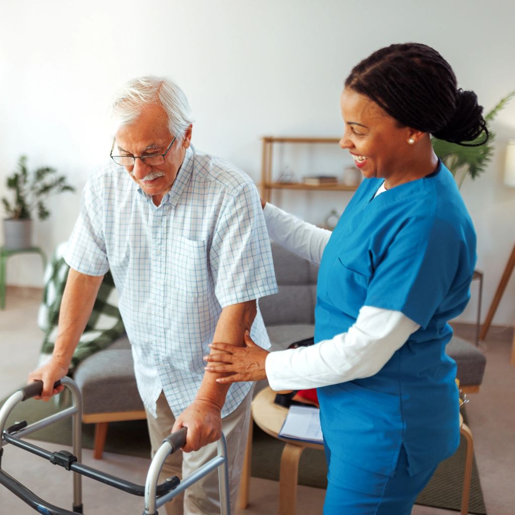 Caregiver smiling while standing next to a man holding a walker.
