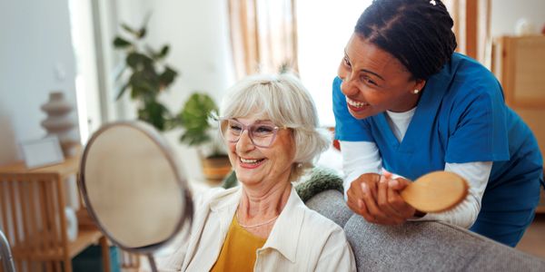 Elderly woman smiling at her reflection while nurse stands behind her.