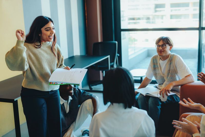 A student confidently presents a project to classmates in a modern classroom environment, with an engaged and attentive audience.
