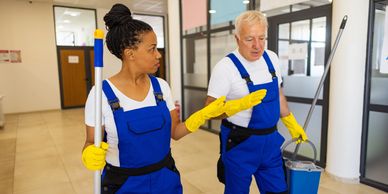 Two janitors in blue uniforms cleaning indoors.