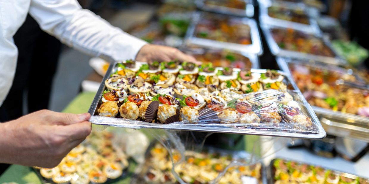 Person holding a tray of assorted gourmet appetizers wrapped in plastic.
