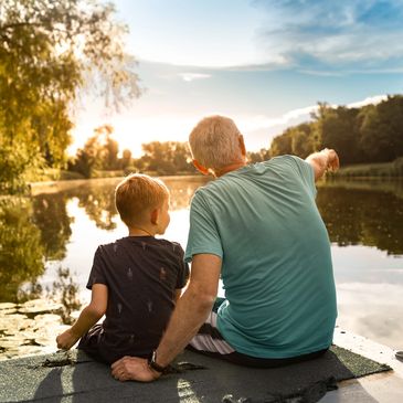 Grandfather and grandson sitting by the lake at sunset.