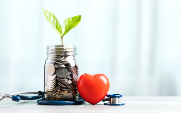 Jar of coins with a plant, a red heart, and a stethoscope on a white surface.