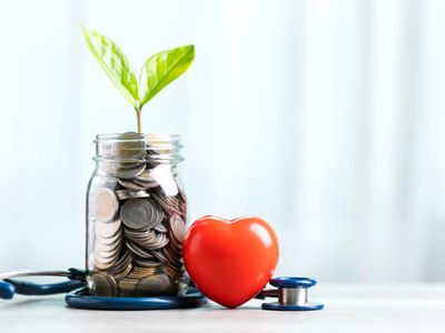 Jar of coins with a plant, a red heart, and a stethoscope on a white surface.