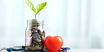 Jar of coins with a plant, a red heart, and a stethoscope on a white surface.