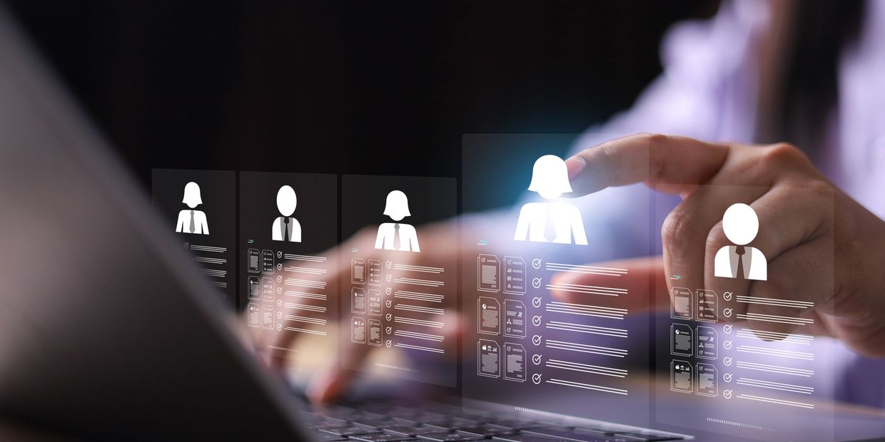 Person selecting a digital profile on a holographic interface above a laptop keyboard.
